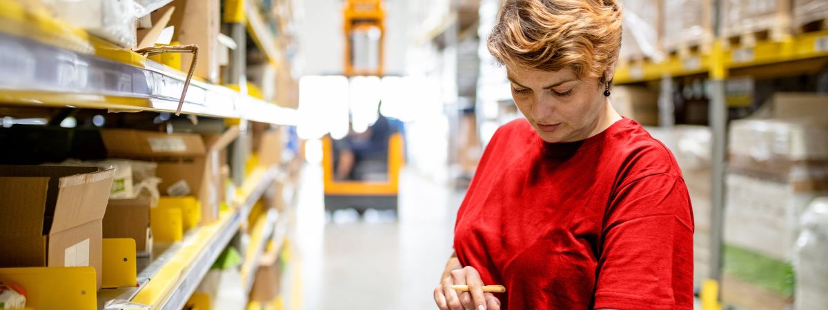 Lagermitarbeiterin beim Scannen vor einem Hochregallager in der Logistikbranche