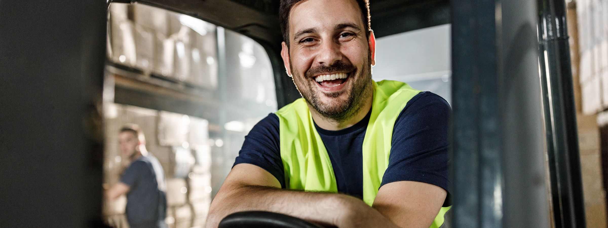 Gabelstaplerfahrer sitzt in einem Gabelstapler und lacht.