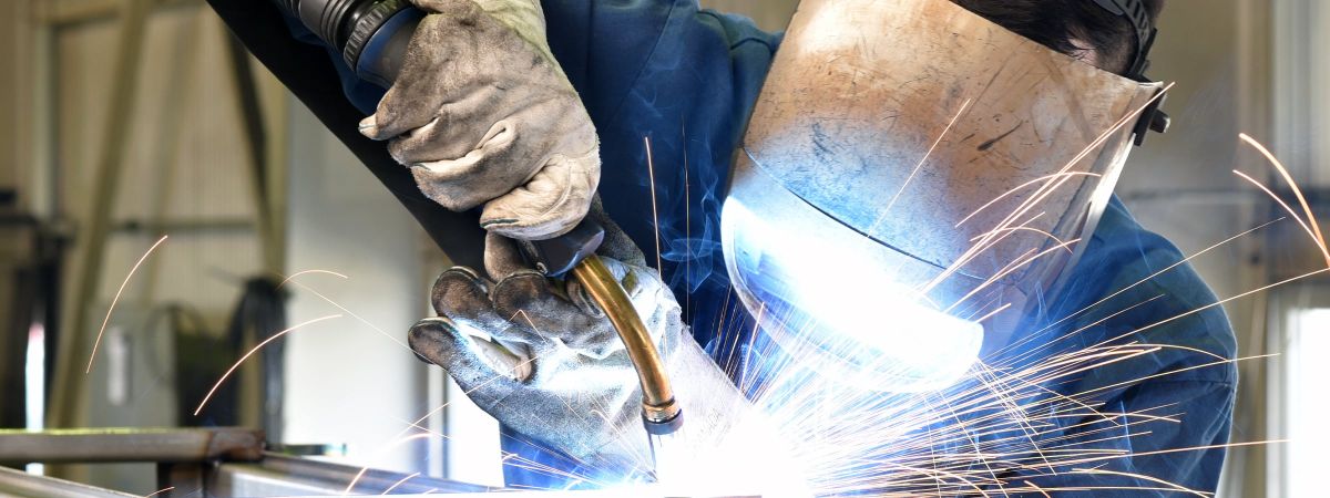 Schweißer im Schutzkleidung, Maske und Handschuhen schweißt Teile zusammen