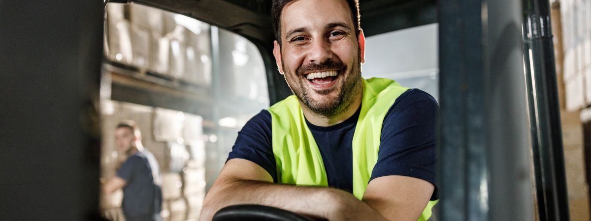 Gabelstaplerfahrer sitzt in einem Gabelstapler und lacht.