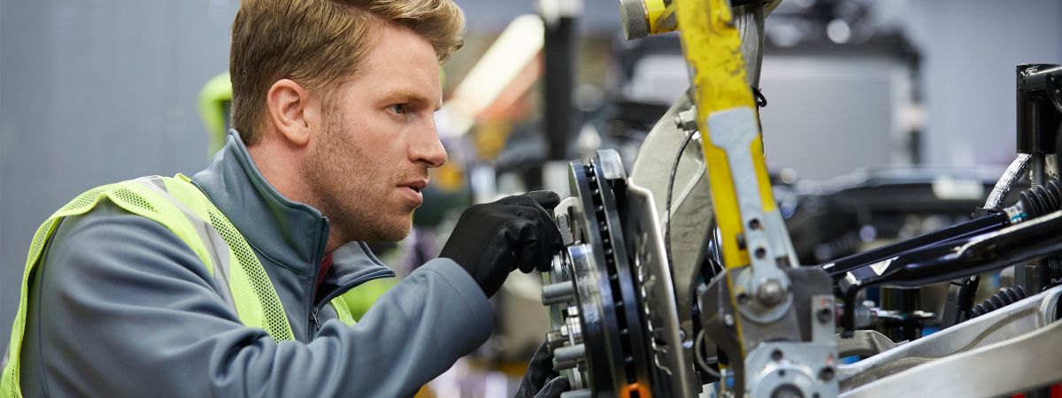 Ein Industriemechaniker in Warnweste und Handschuhen arbeitet konzentriert an einer Maschine in einer Produktionshalle.