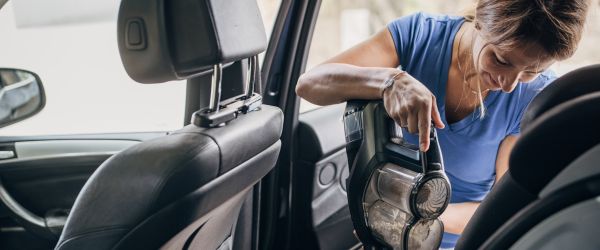 Frau reinigt mit einem handstaubsauger die Rücksitze im Auto